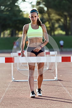 Young athlete jumping over a hurdle during training on race trac