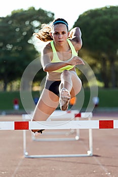 Young athlete jumping over a hurdle during training on race trac