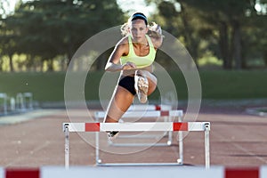 Young athlete jumping over a hurdle during training on race trac