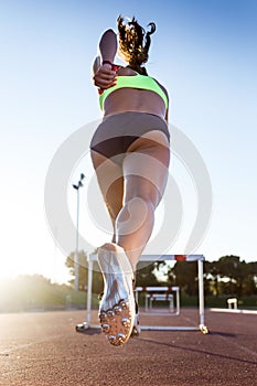 Young athlete jumping over a hurdle during training on race trac