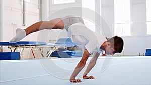 A young athlete is making a side split in a handstand, arms straight, side view.