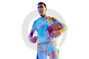 Young athlete man in basketball uniform holds ball and shouting clenching fists of happiness against white studio