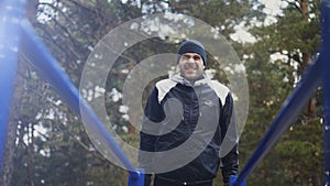 Young athlete man doing push-ups exercise on bars in winter park outdoors