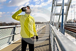 Young athlete man drinking water - rehydrating during exercise outdoors