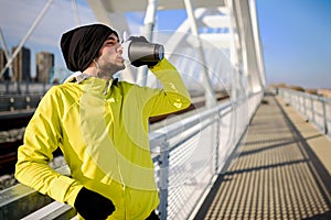 Young athlete man drinking water - rehydrating during exercise outdoors