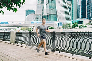 Young athlete man runner running at summer morning, background urban city street. Sports training. Fitness cardio