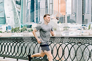 Young athlete man runner running at summer morning, background urban city street. Sports training. Fitness cardio