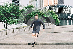 Young athlete man runner running up stairs on city stairs in summer on morning run, background urban city street. Sports