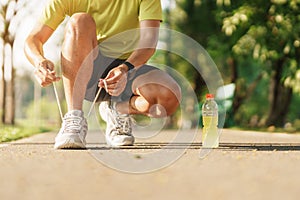 Young athlete man tying running shoes with Energy Drink water, male runner ready for jogging outside, asian Fitness walking and