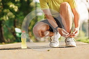 Young athlete man tying running shoes with Energy Drink water, male runner ready for jogging outside, asian Fitness walking and