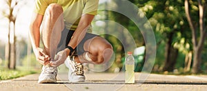 Young athlete man tying running shoes with Energy Drink water, male runner ready for jogging outside, asian Fitness walking and