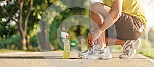 Young athlete man tying running shoes with Energy Drink water, male runner ready for jogging outside, asian Fitness walking and