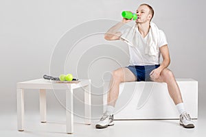 Young athlete with towel drink water after workout on grey background