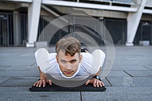 Young athlete training outdoors, push up, look at camera