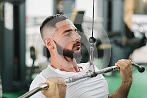 A young athlete trains in the gym. Male trains the muscles of the back and chest