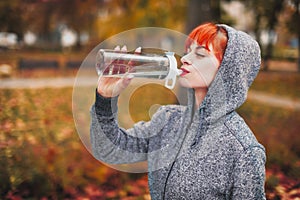 Young athlete woman drinking water from bottle during outdoor preparation in park