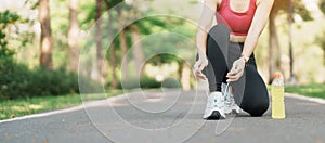 Young athlete woman tying running shoes with Energy Drink water, female runner ready for jogging outside, asian Fitness walking