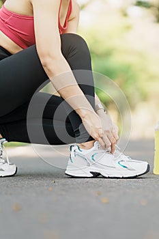 Young athlete woman tying running shoes with Energy Drink water, female runner ready for jogging outside, asian Fitness walking