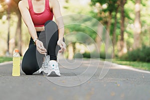 Young athlete woman tying running shoes with Energy Drink water, female runner ready for jogging outside, asian Fitness walking