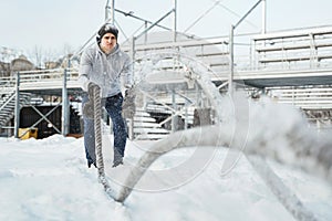 Young athlete working out with a battle ropes during snowy winter day.