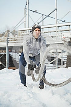 Young athlete working out with a battle ropes during snowy winter day.