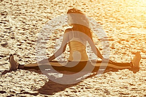 Young athletes - gymnast with curly hair and sneakers doing the splits on the beach in summer morning exercise.