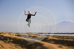 Young athletic and attractive crazy happy woman jumping high on the air at beautiful beach enjoying freedom and nature during