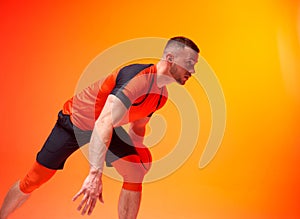 Young athletic basketball player in attack position holding ball with one hand on orange and red background