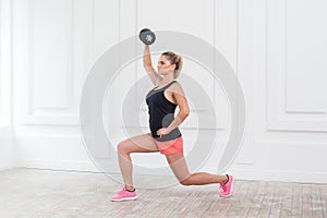 Young athletic beautiful blonde woman wearing pink shorts and black top holding dumbbell.