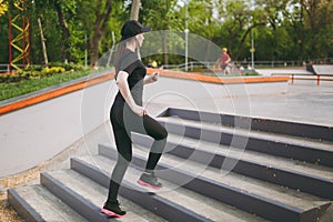 Young athletic beautiful brunette girl in black uniform, cap with headphones doing sport exercises, training and running