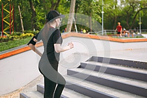 Young athletic beautiful brunette girl in black uniform, cap with headphones doing sport exercises, training and running