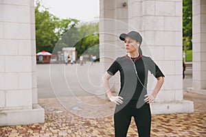 Young athletic beautiful brunette girl in black uniform, cap with headphones doing sport exercises, warm-up before