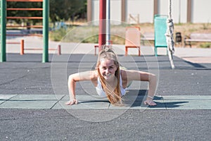 Young, athletic and beautiful girl doing push-ups on the sports ground.