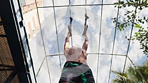 Young athletic boy doing exercise on the gymnastic rings at street workout place. Young athlete doing pull-ups on