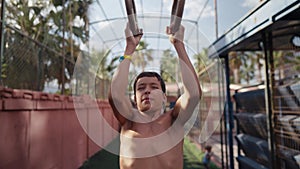 Young athletic boy doing exercise on the gymnastic rings at street workout place. Young athlete doing pull-ups on