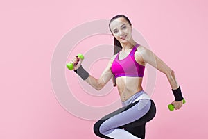 Young athletic brunette girl in a bright sports top and with a ponytail, runs with green dumbbells and hair fluttering.