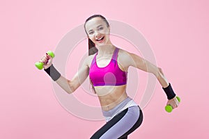 Young athletic brunette girl in a bright sports top and with a ponytail, runs with green dumbbells and hair fluttering.
