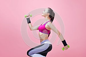 Young athletic brunette girl in a bright sports top and with a ponytail, runs with green dumbbells and hair fluttering.