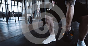 Young athletic Caucasian sportsman lifting kettlebell during hardcore physical workout training in large gym slow motion