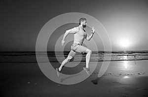 Young athletic and fit american sport man doing running workout on sunset at the beach training jogging barefoot in
