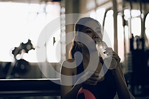 Young athletic fitness woman drinking water from bottle  in gym