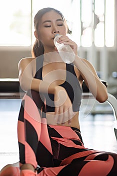 Young athletic fitness woman drinking water from bottle  in gym