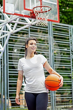 Young athletic girl is training to play basketball on modern outdoor basketball court. Happy woman
