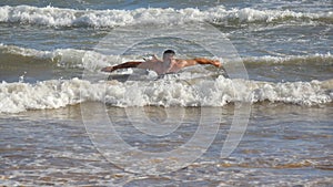 Young athletic guy paddling out at ocean wave and learning to surfing during summer trip on sunny day. Concept of