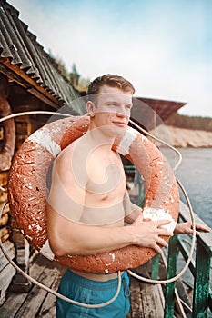 This is a young athletic guy in shorts and bare-chested standing with an old lifebuoy.