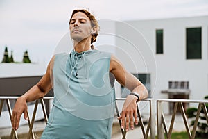 Young athletic long-haired man in headphones relaxing with closed eyes