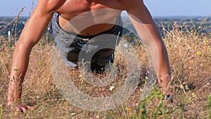 Young athletic man with a bare torso performs pushups on the nature