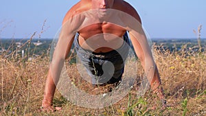 Young Athletic Man with a Bare Torso Performs Pushups on the Nature