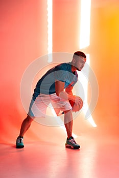 Young athletic man, basketball player dribbling with ball on red and orange background