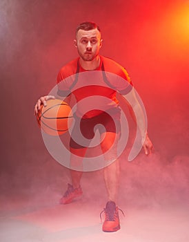 Young athletic man, basketball player preparing for throwing the ball with back lights and smoke on background